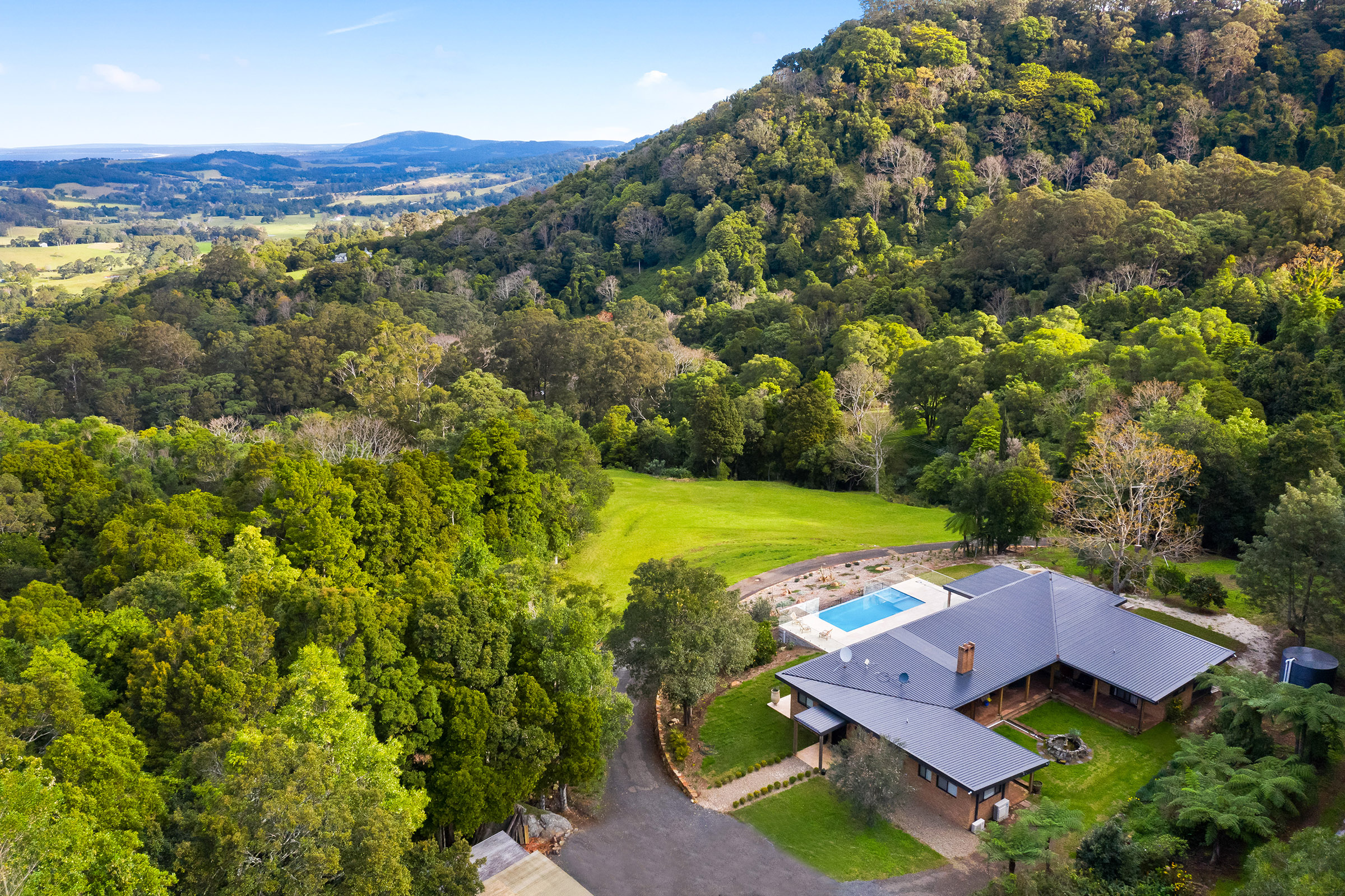 An elevated view of a modern farmhouse in Foxground, NSW, nestled among lush greenery with expansive outdoor living, built by Lime Building Group.